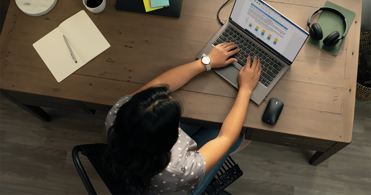 Top down photo of a person working at a desk with Lenovo ThinkPad X1 Yoga laptop and extra monitor