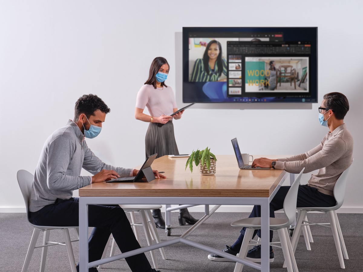 Coworkers setting up a PowerPoint presentation for a Microsoft Teams meeting in a conference room
