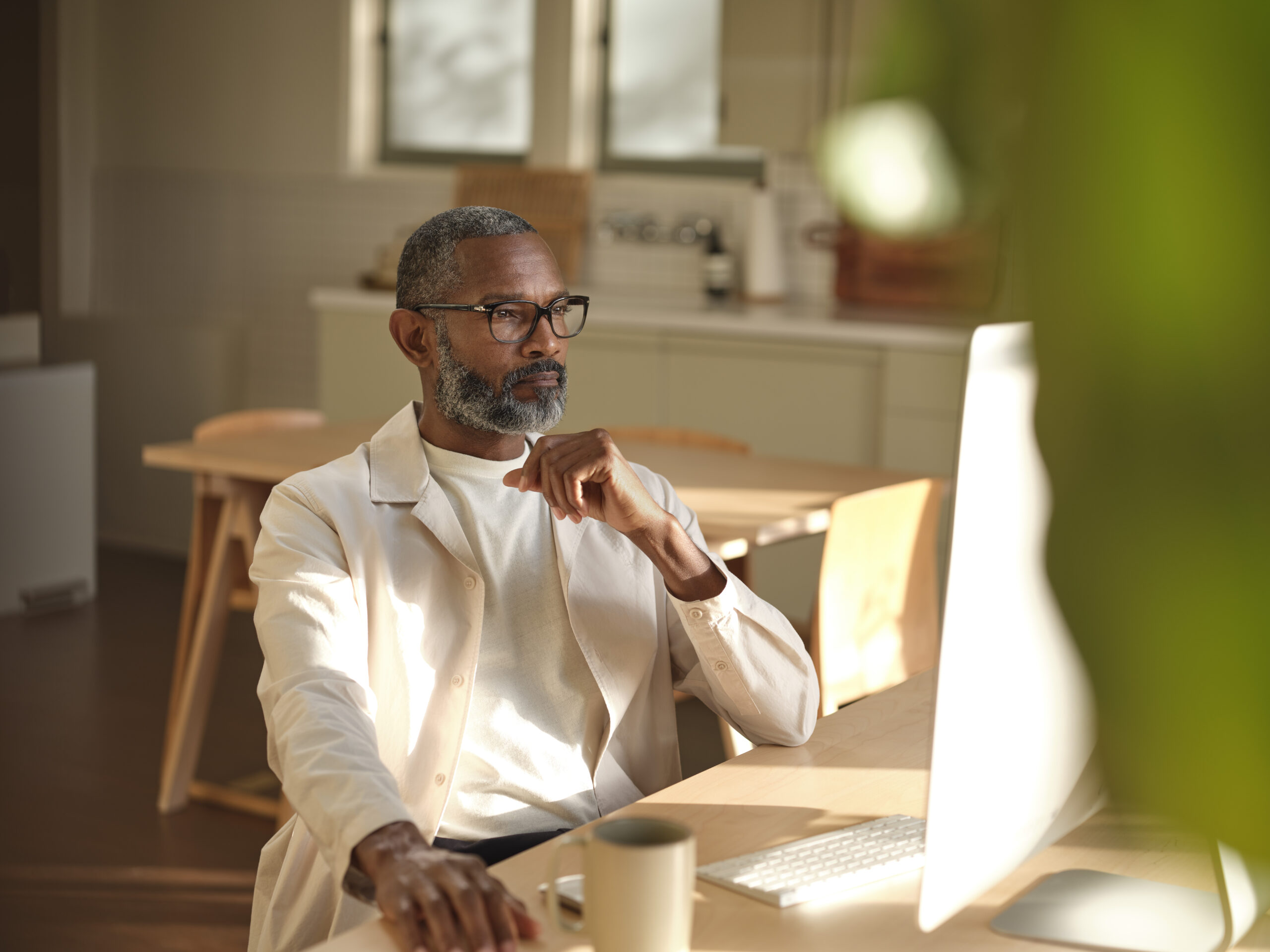 Man sitting at wooden table looking at the the screen on a desktop computer