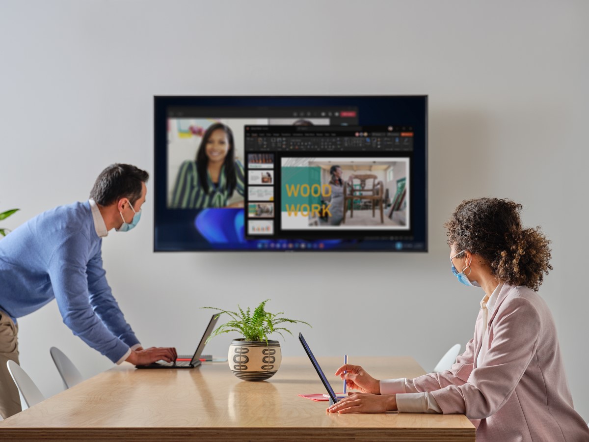 Coworkers with masks setting up a Microsoft Teams meeting in a conference room with their HP Elite Folio Notebooks