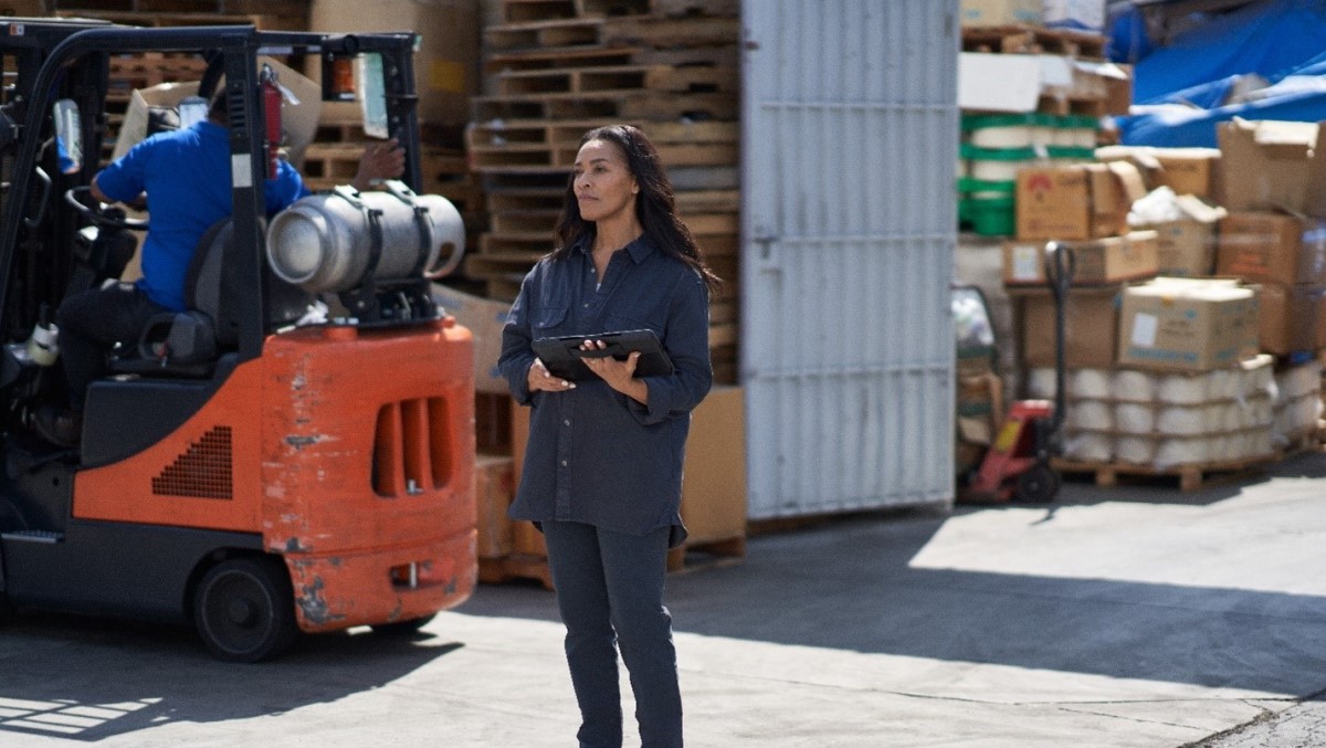 Female manufacturing worker holding tablet device while monitoring work outside of a factory