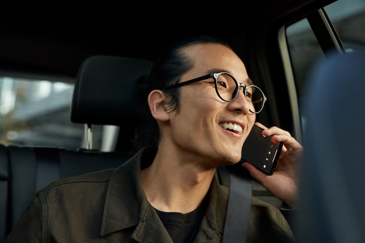 A man talking on his mobile phone, using Teams phone, while sitting in the backseat of a vehicle​