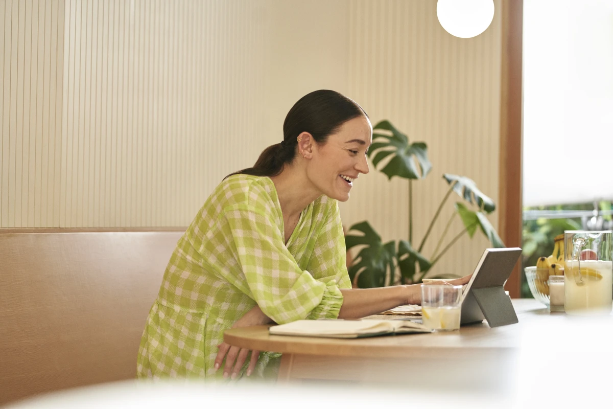Woman sitting in kitchen working on 2-in-1 tabletin laptop mode