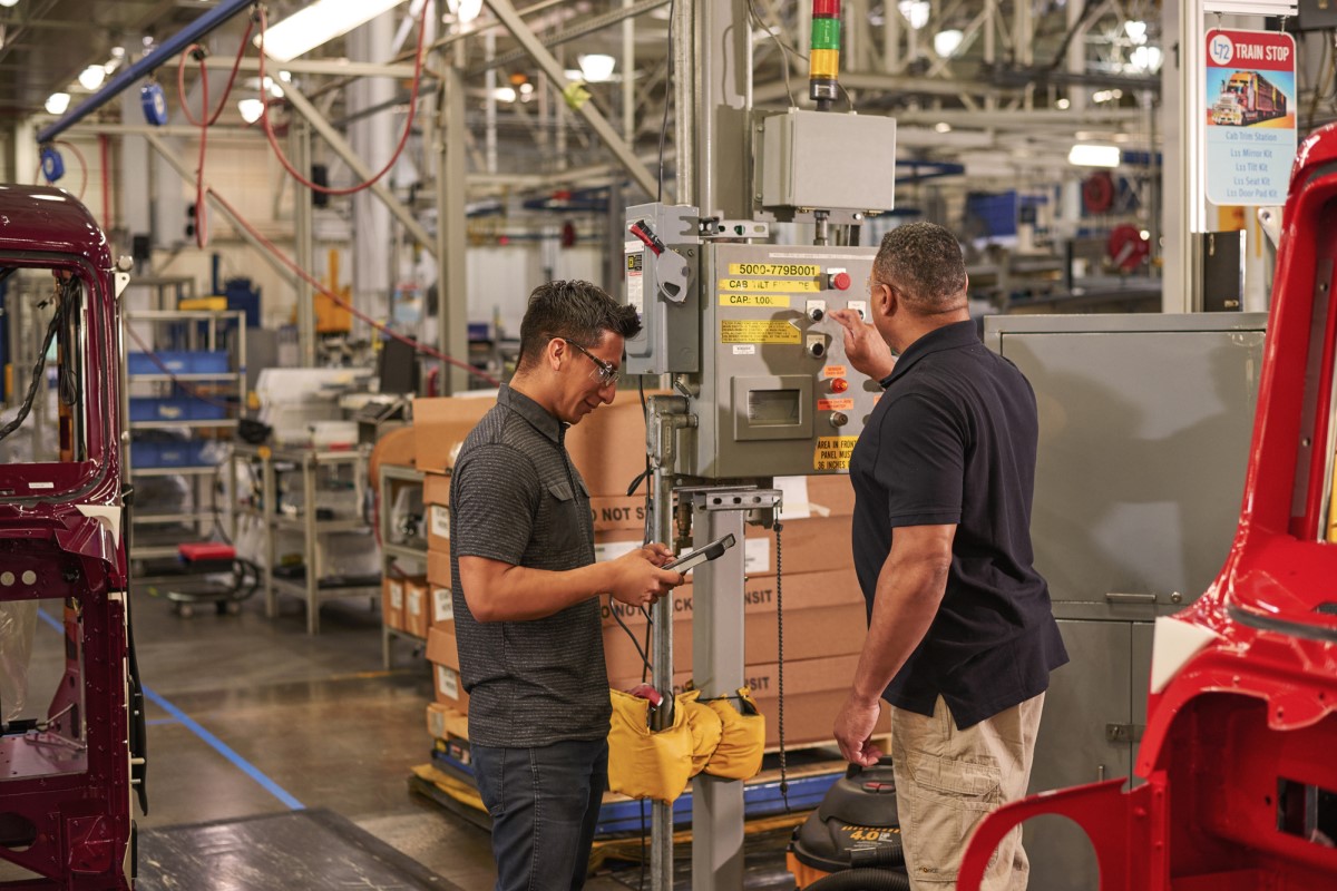Two engineers wearing safety goggles use machinery at a manufacturing plant