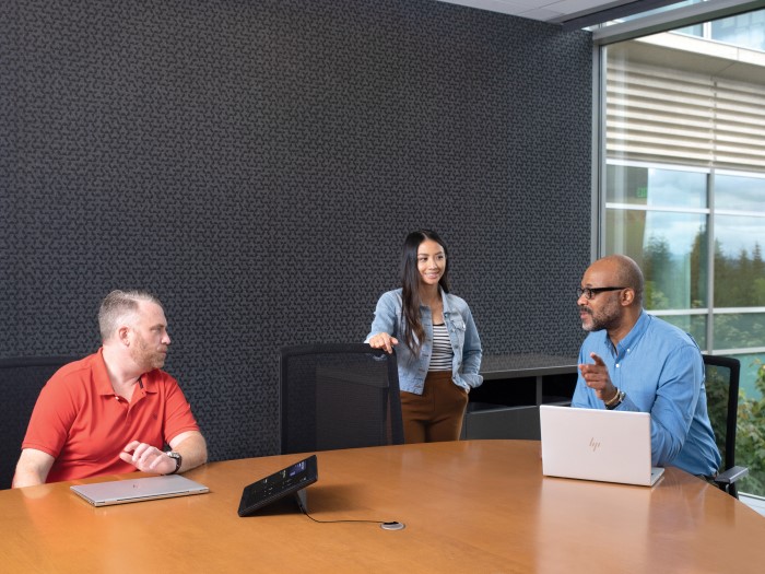 One female and two males in medium conference room with an HP Slice Microsoft Teams Rooms touch display and two HP laptops in view