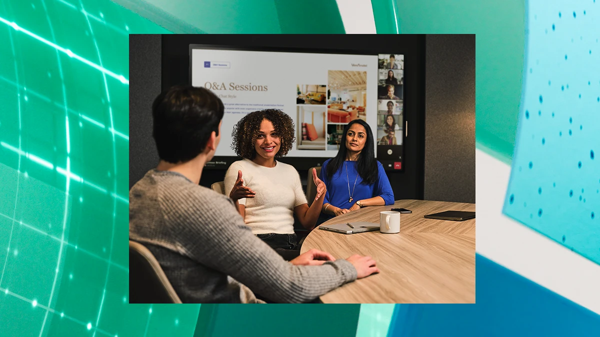 A photo of three people sitting at a conference room table, talking, with a presentation on a screen behind them. The photo is overlaid on a green and blue graphic design background
