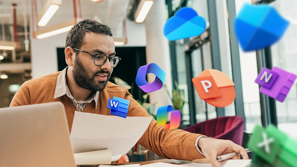 An financial advisor works at a table in a shared office space. On the right side, the image is overlaid with icons of multiple Microsoft 365 apps and the Copilot icon