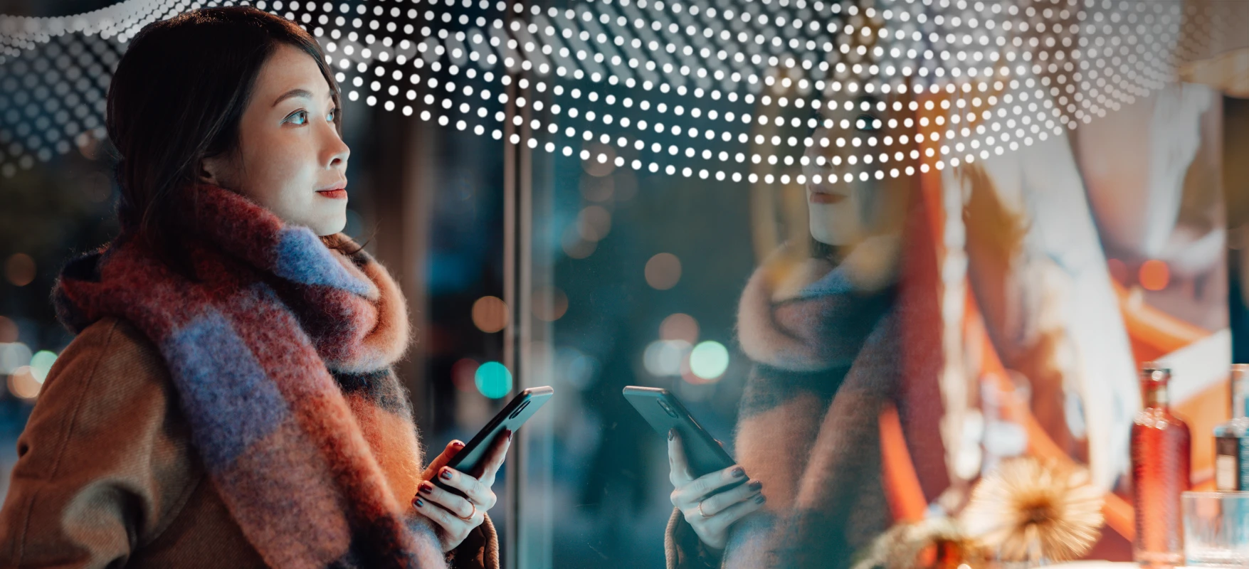 Woman holds cell phone in front of retail storefront display with merchandise at night