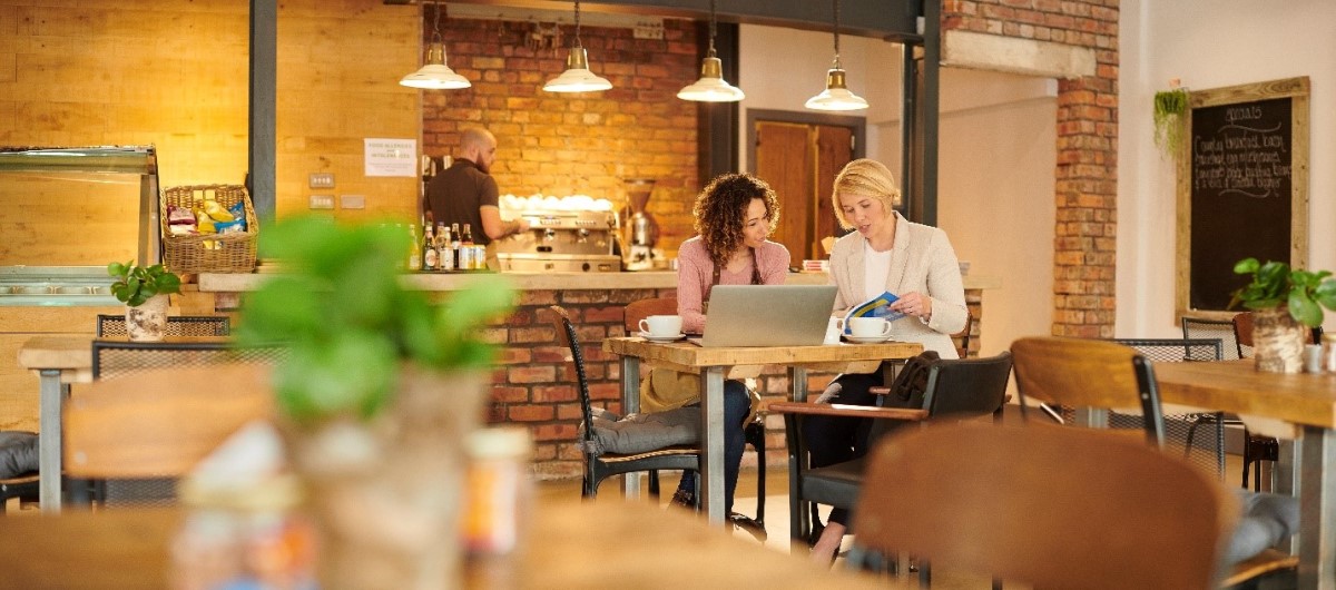 Interior: warmly lit exposed brick cafe. Financial advisor sits with new business owner