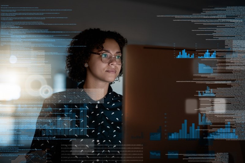 Shot of A person wearing glasses works at a computer screen. Images of data and charts overlay the image to infer what the person is working on at the computer console
