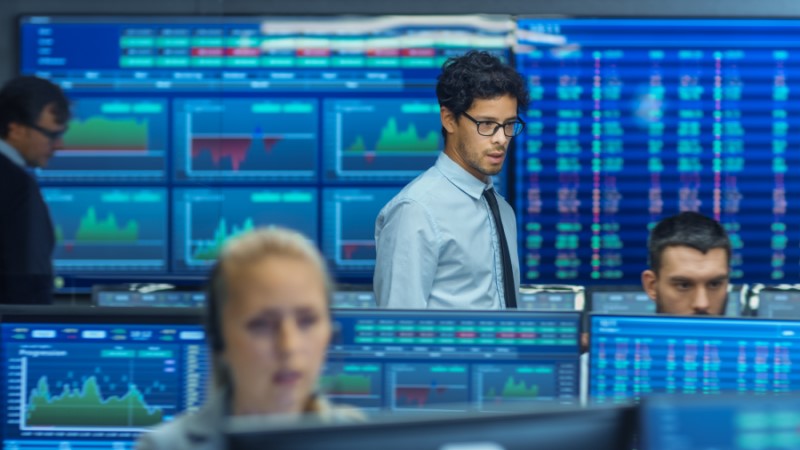 : people in room reviewing multiple screens with charts and financial information on them