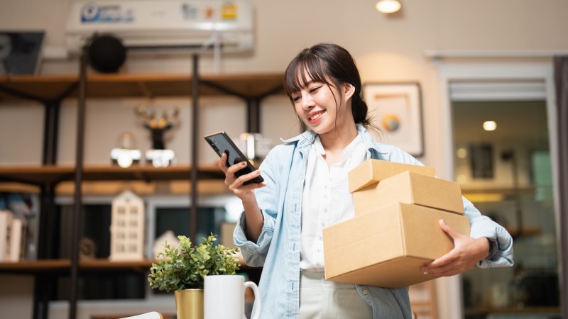 woman shopping while holding packages and looking at her device