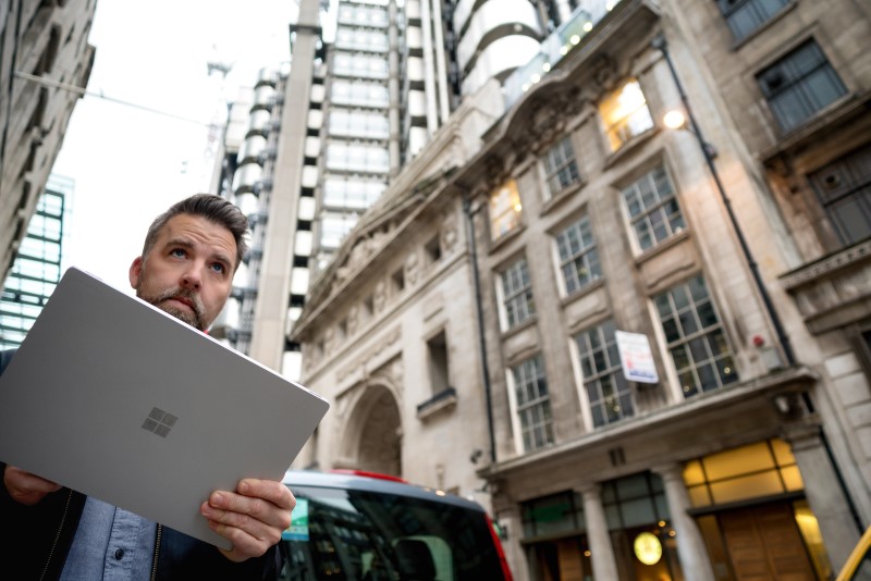 Male commuter holding Microsoft tablet (screen not shown). He is standing on city street, looking over tablet