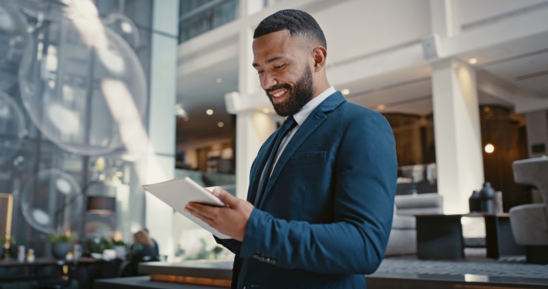A smiling man standing in a lobby looking at a tablet