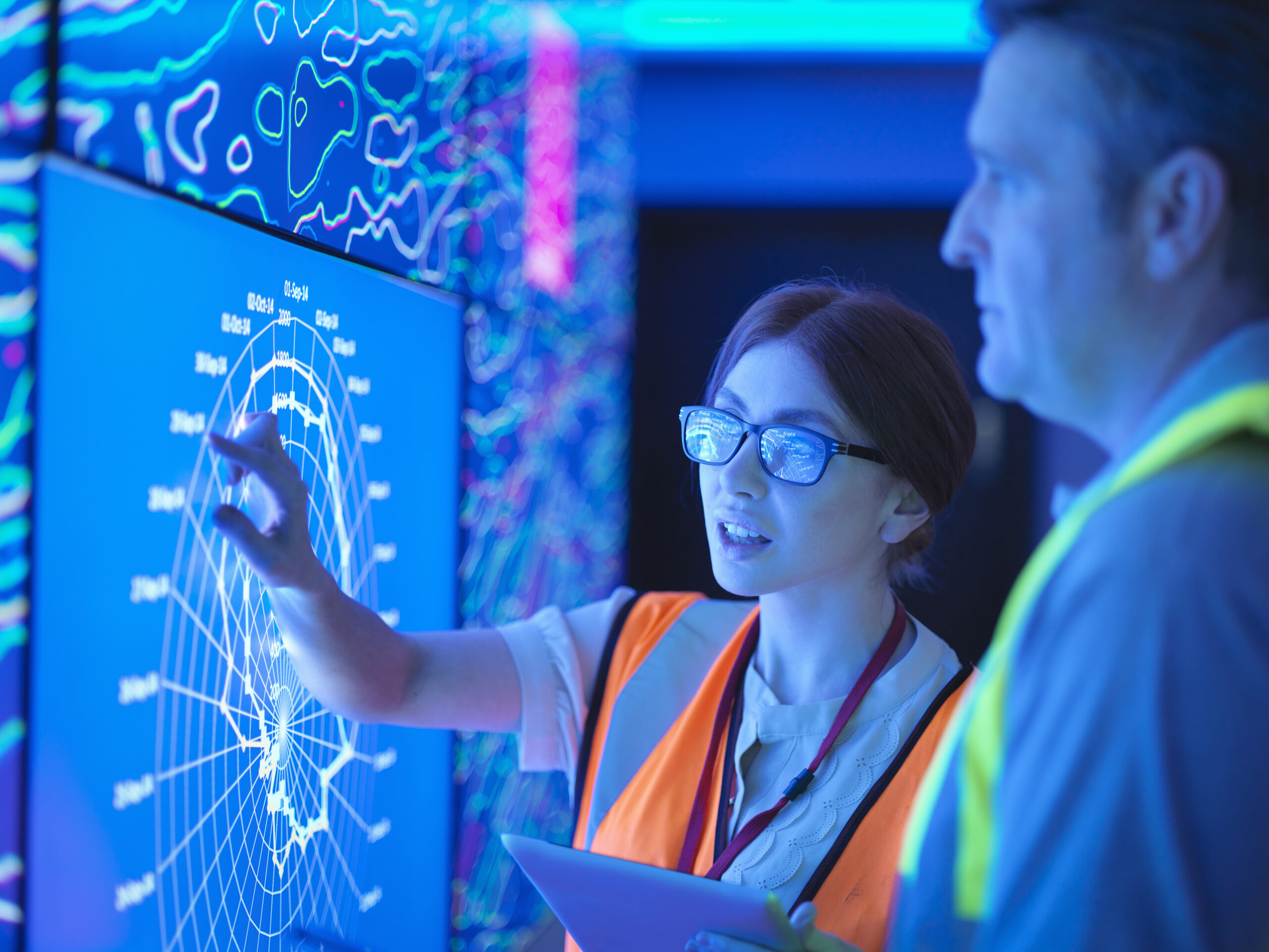 Female geologist with colleague studying graphical display of oil and gas bearing rock on screens