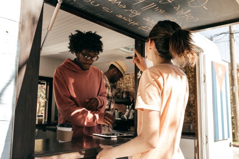 Owner of a food truck help a customer, and takes an order for coffee using a digital tablet