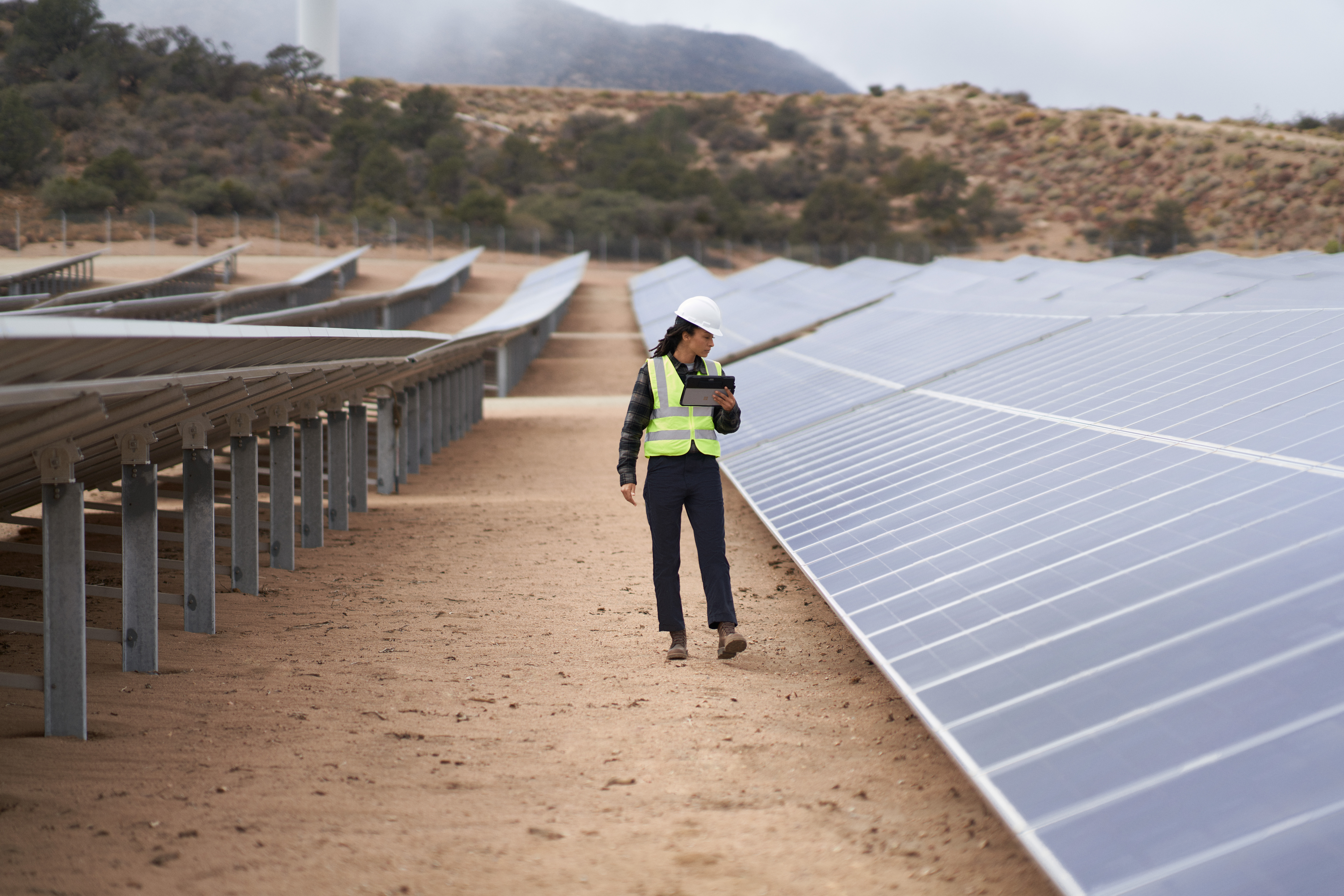 Field engineer inspects solar panels on a wind farm using remote assist with a Surface tablet