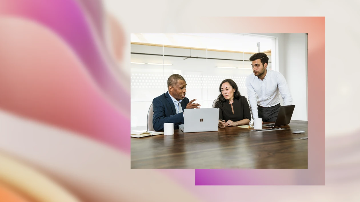 Two male and one female corporate office workers sitting at conference room table in discussion. There are two open laptops on the table