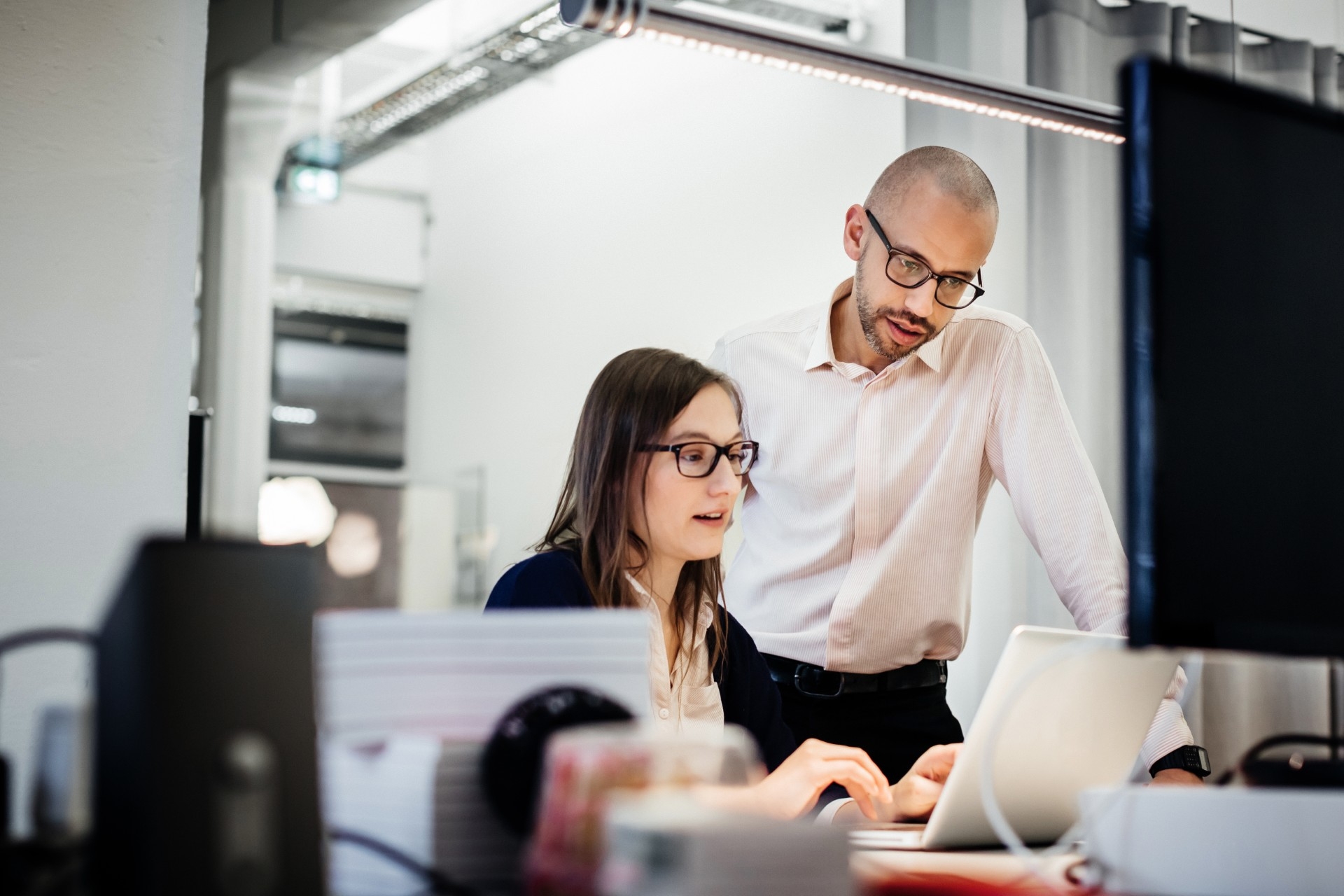 Two professionals collaborating at a desk, reviewing information on a laptop screen in a modern office setting