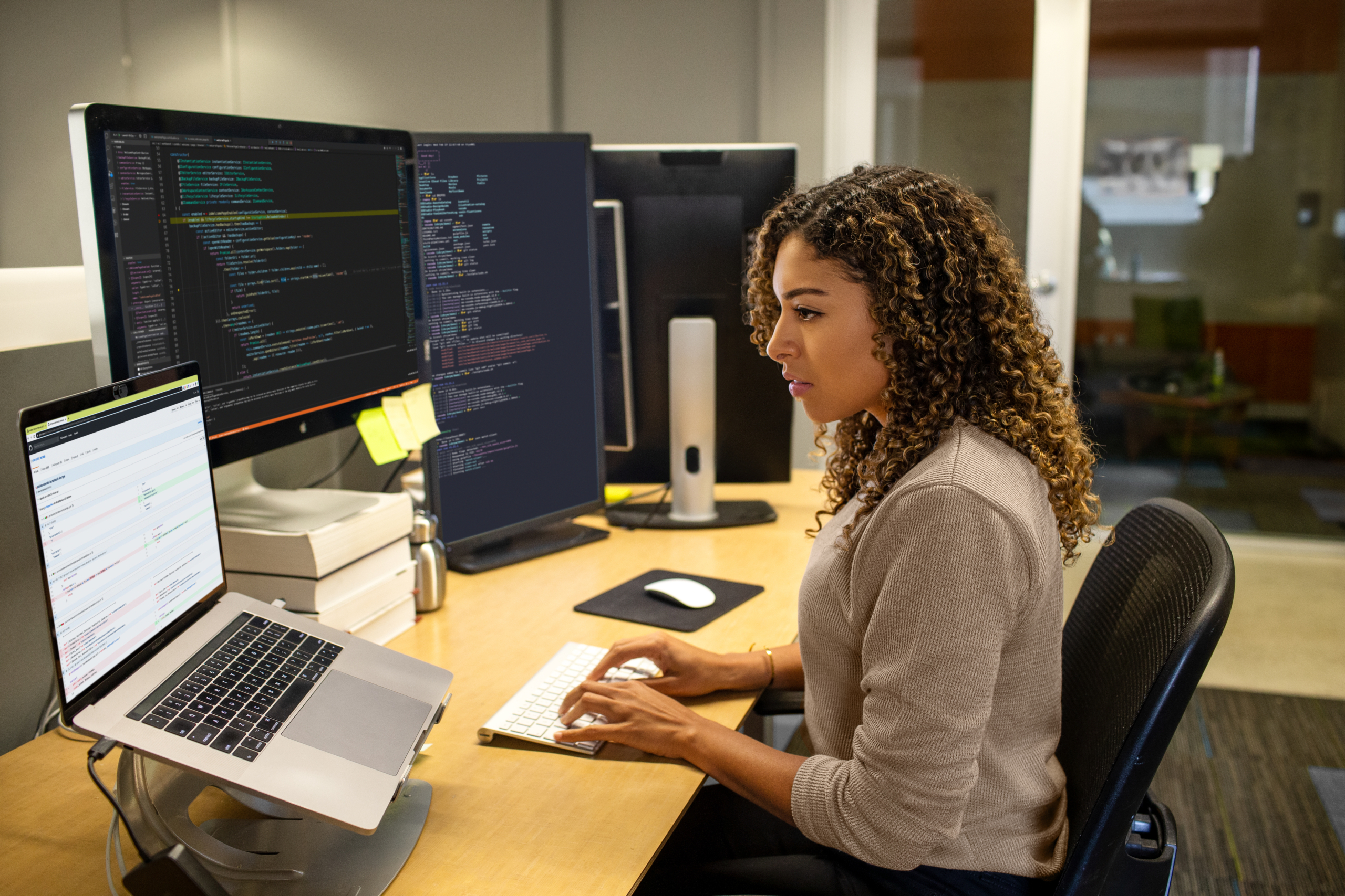 Real people, real offices. Black female developer working at enterprise office workspace. Focused work. She has customized her workspace with a multi-monitor set up. Women who code, women developers, women engineers, code, develop, Black developer, engineer, Visual Studio, Azure