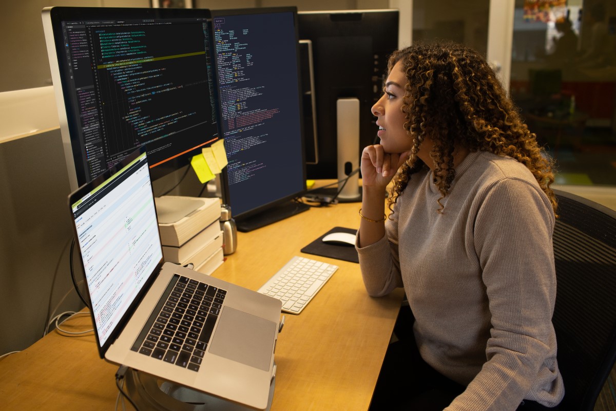 Female developer coding at her desk. She has customized her workspace with a multi-monitor set up and using Visual Studio for Mac