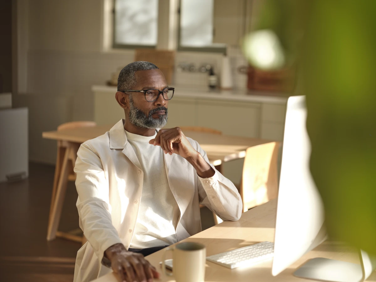 Man sitting at wooden table looking at the the screen on a desktop computer