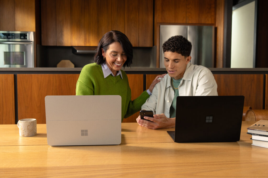 Two individuals and their laptops discussing at a kitchen table.