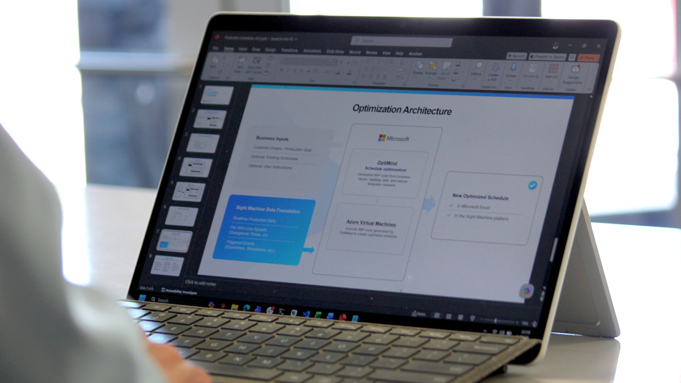 Laptop displaying a presentation slide titled “Optimization Architecture,” showing a workflow from business inputs through Microsoft Azure and OptiMind schedule optimization to a new optimized schedule output.