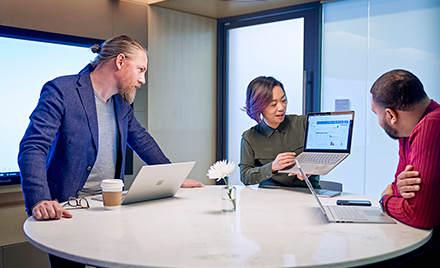 Image of three coworkers gathered around a laptop