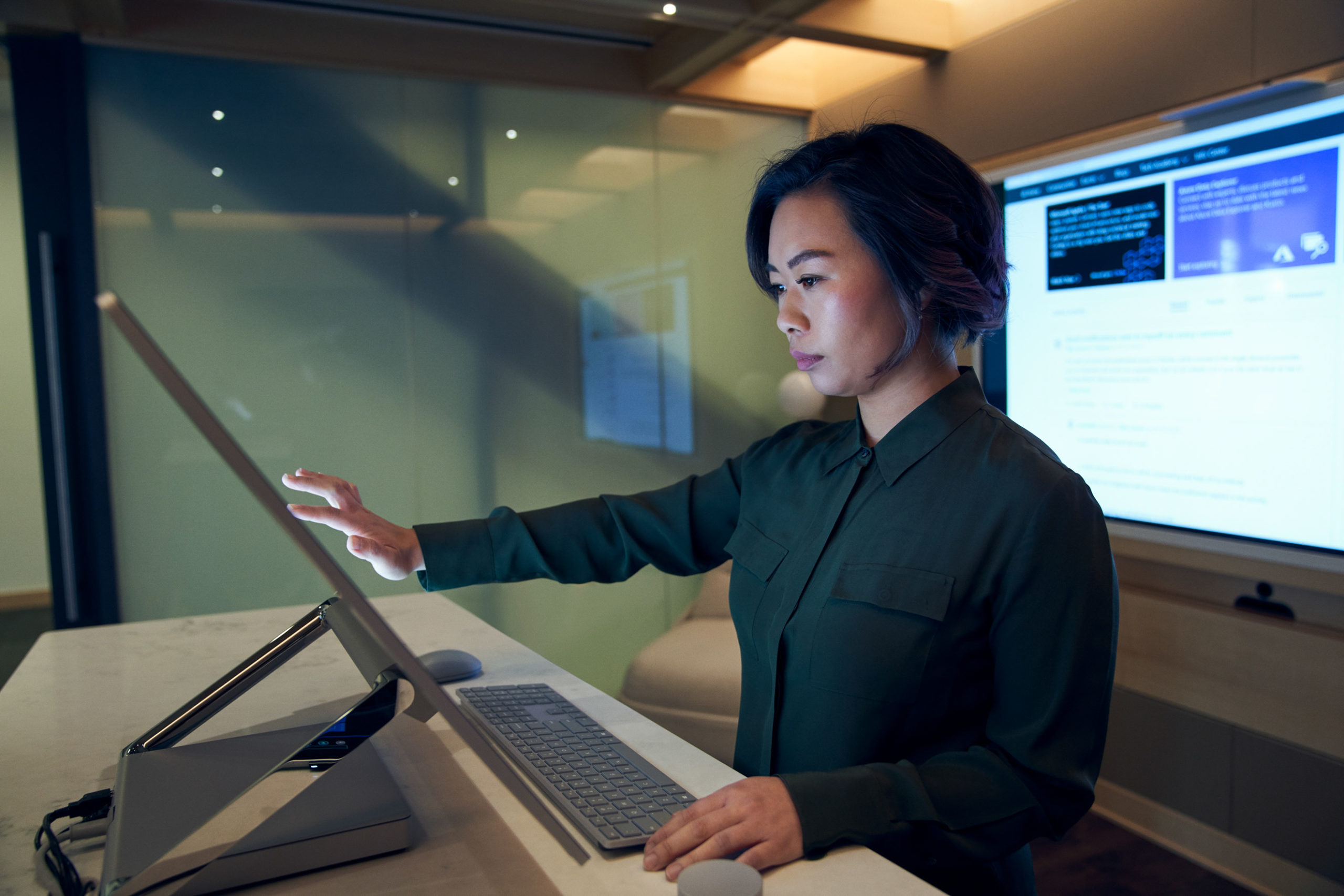 Side profile of a woman wearing a dark shirt in a dim office scrolling or working on a Microsoft Surface Studio