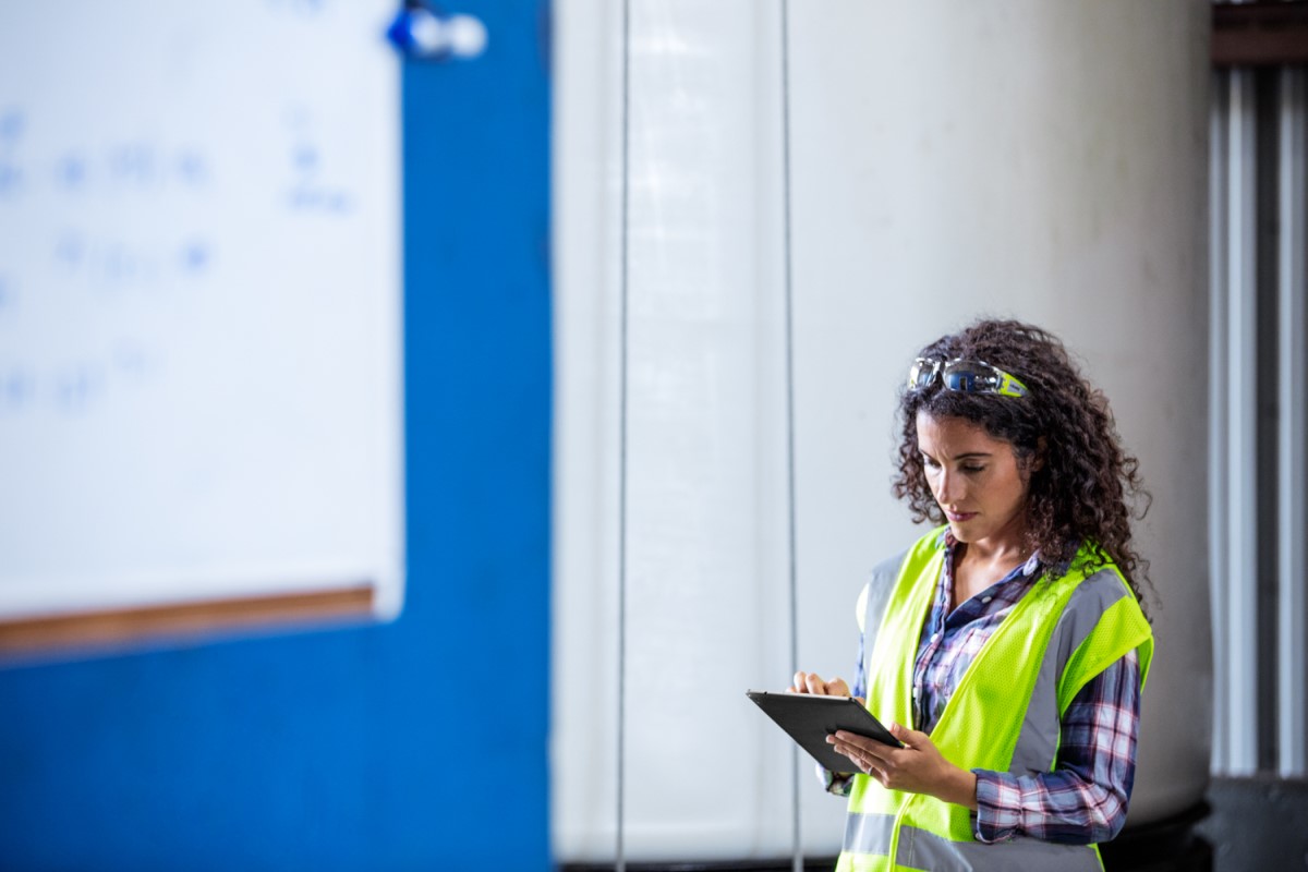Female worker wearing neon vest and safety glasses using tablet