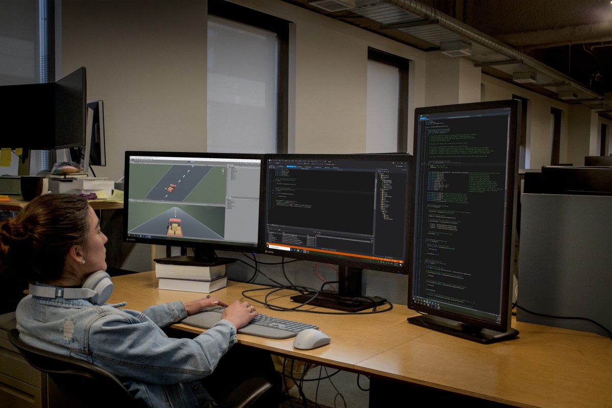 Real people, real offices. Female developer coding at her PC workspace in an enterprise office using Visual Studio on a multi-monitor set up