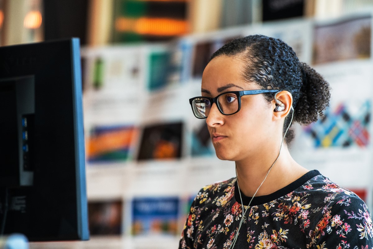 Adult woman works at computer station with headphones in
