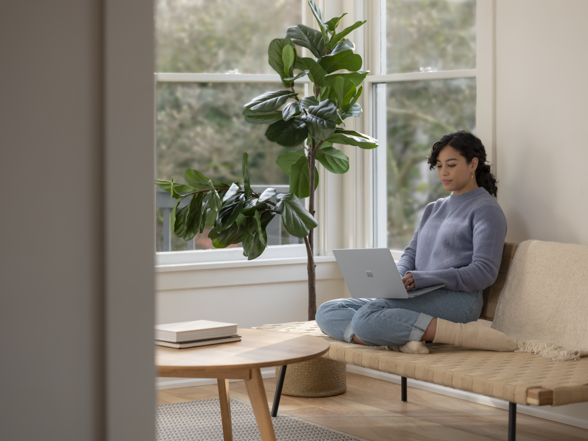 Adult female sitting on couch inside working on Surface Laptop