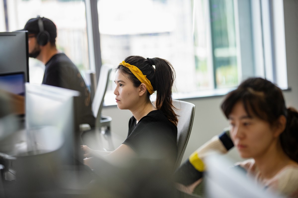 An employee in the tech industry works at a shared desk with other employees in their office