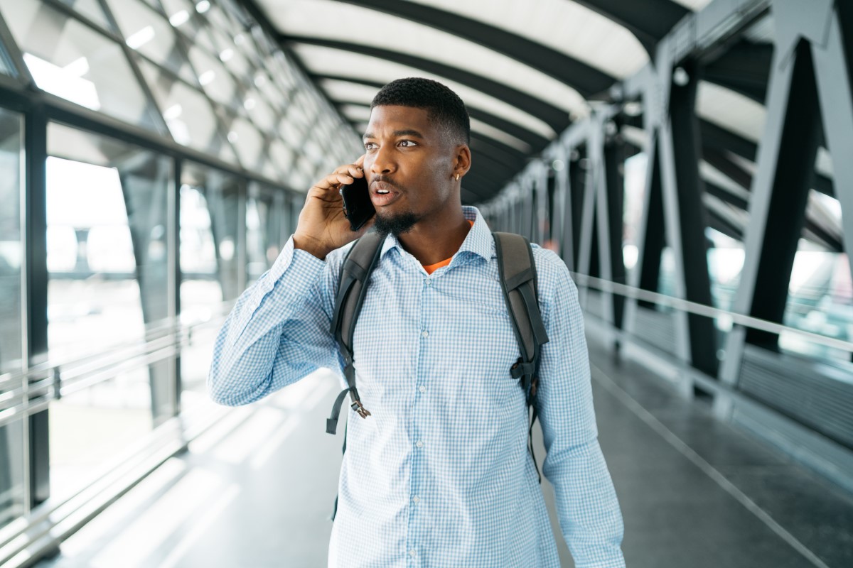 A young man walks through an airport talking on the phone