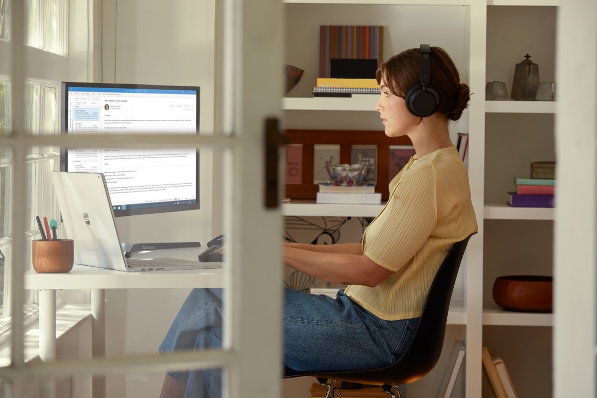 Female inside working in Outlook on Surface Book 3 and wearing Surface Headphones 2