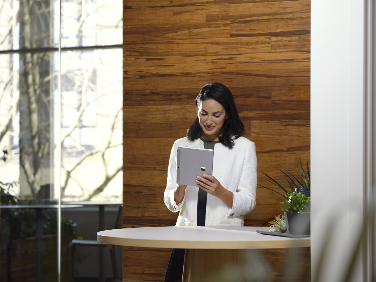 Adult female holding a platinum Surface Go 3 in tablet mode while in an office setting