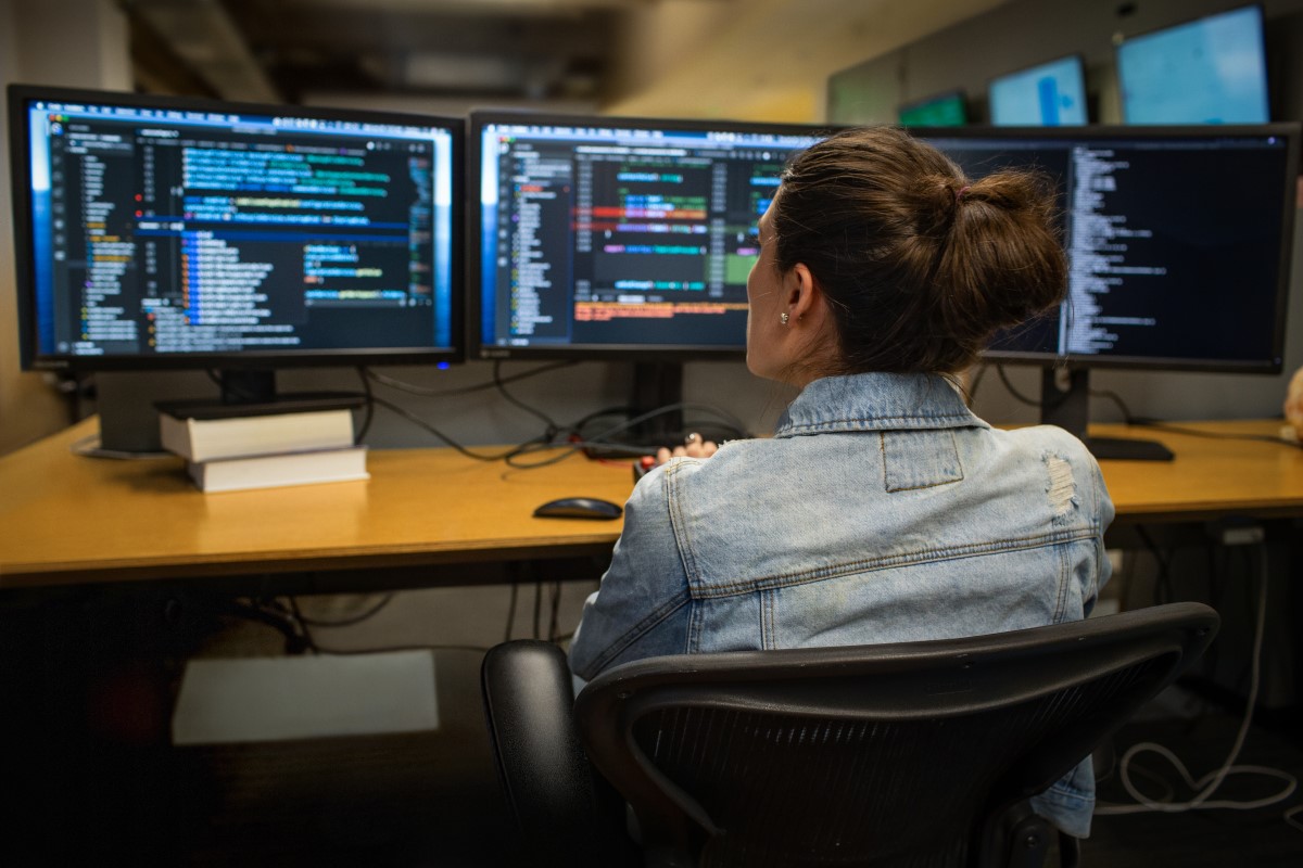Female developer coding her workspace in an enterprise office, using Visual Studio on a multi-monitor set up