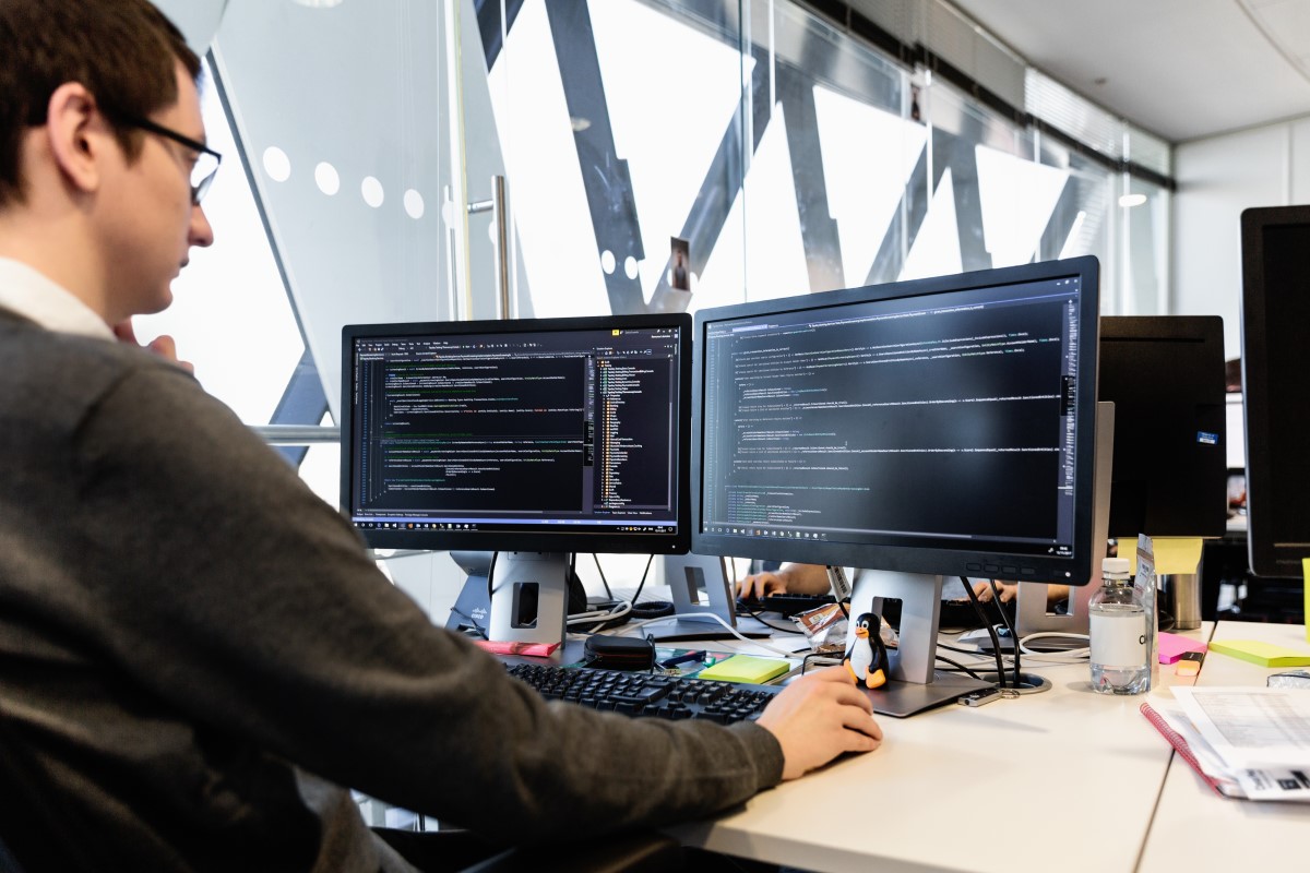 Male developer coding in front of two monitors at desk in office