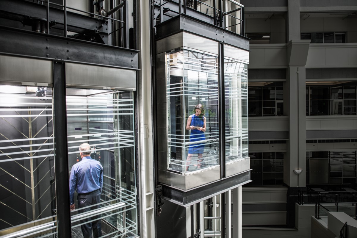 Business woman and man in separate glass elevators. The woman is using a Surface Pro