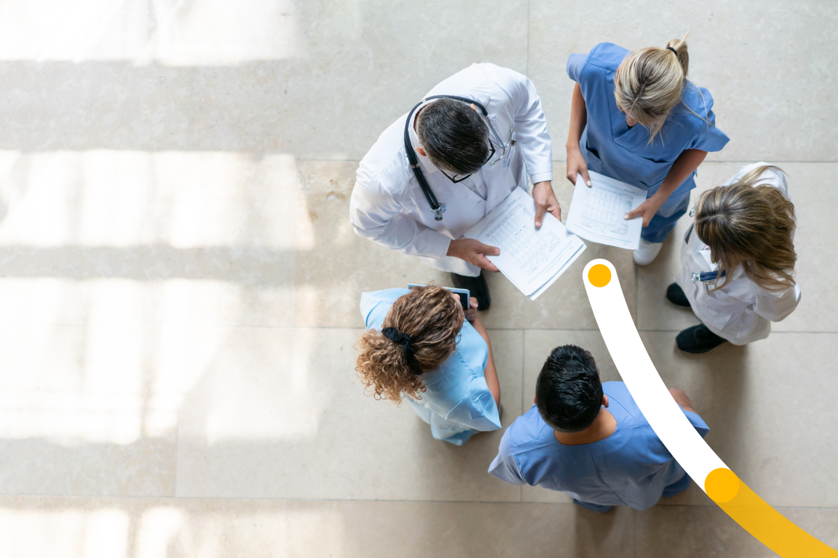 Five medical professionals standing in a circle reviewing a chart