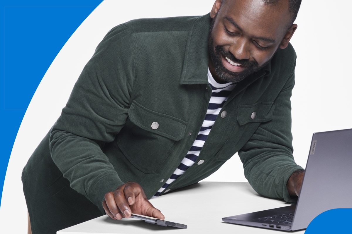 Photograph of adult male looking at Lenovo IdeaPad and mobile phone photographed in studio on white background