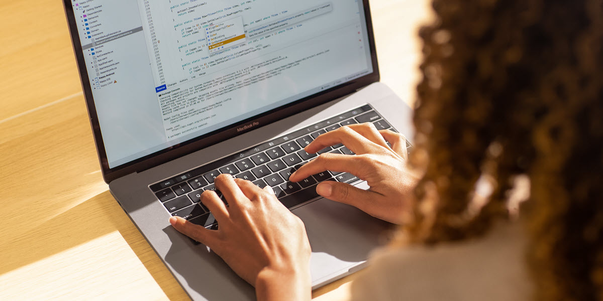 Black female developer coding on a MacBook Pro in the office, using Visual Studio