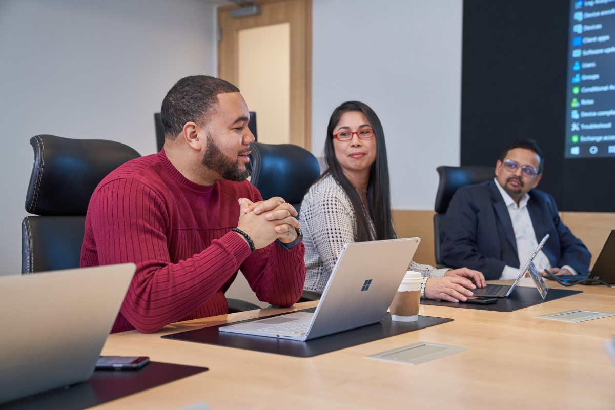 Group of people at a conference table with laptops who appear to be have a healthy and positive discussion or meeting