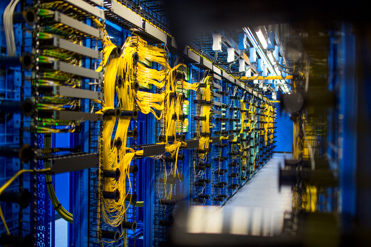Data center illuminated with a bluish light. Yellow cords running on the servers are prominently displayed