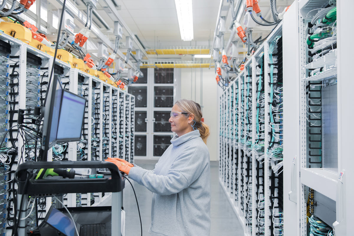 Female datacenter employee performs maintenance in datacenter cold aisle