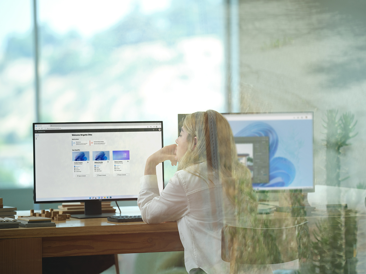 A female architect sitting at an office desk showing Windows 365 and its Welcome screen on dual desktop monitors. Shown on Windows 11