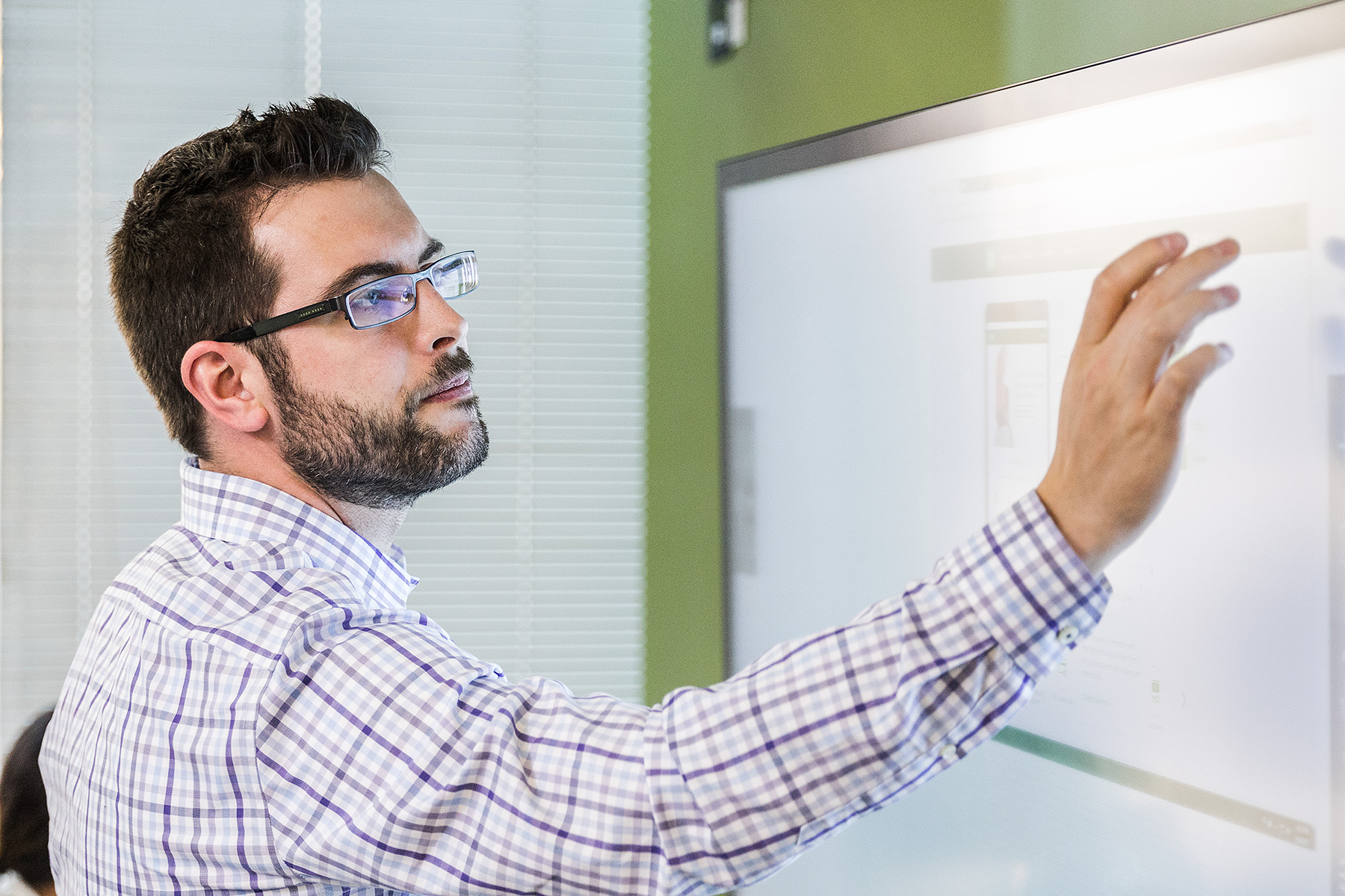 Male office worker standing in modern office and using large touchscreen monitor with right hand (screen shows open browser window)