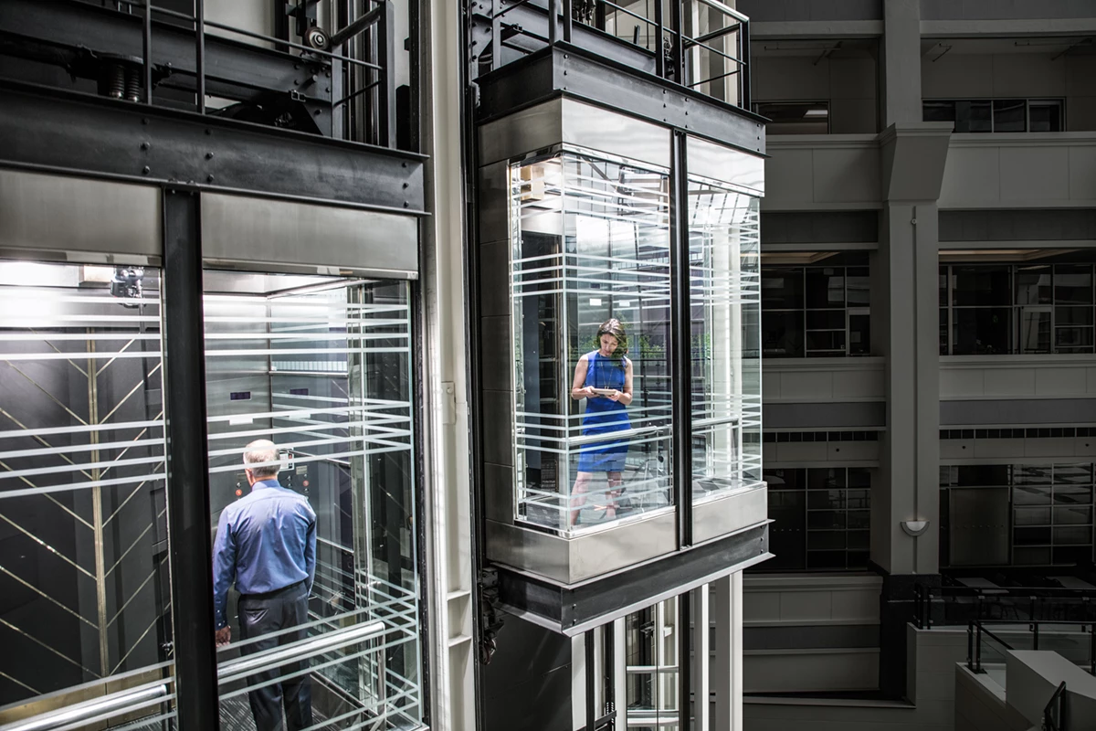 Photo of business woman and man in separate glass elevators